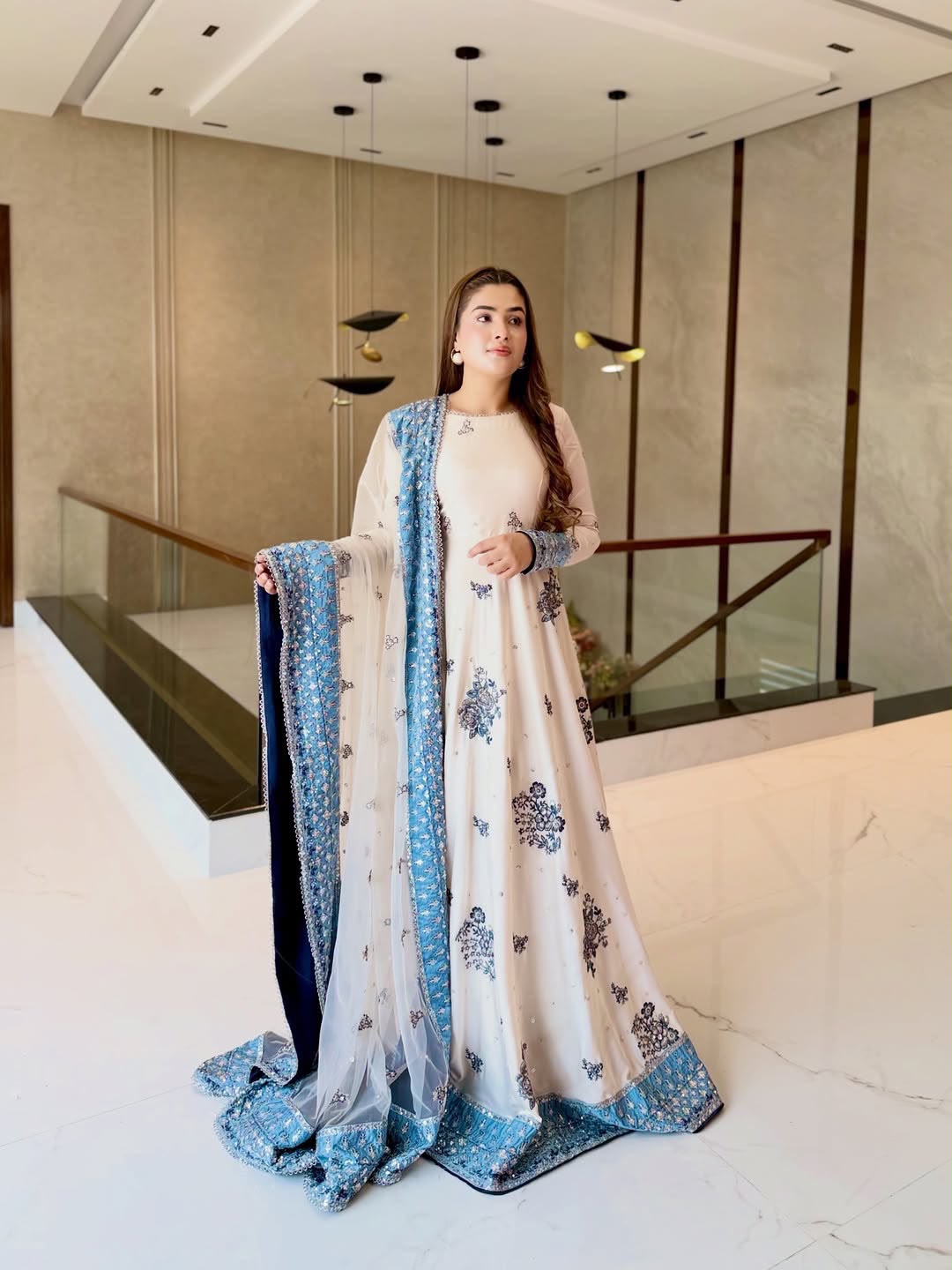 Model in ivory star georgette embroidered gown with sky blue dupatta standing on staircase
