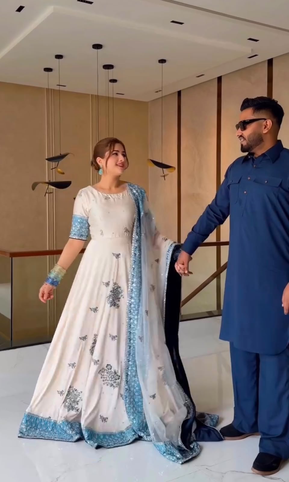 Couple holding hands in ivory embroidered gown showing sky blue hem border and cuffs